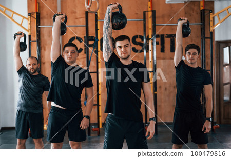 Lifting of heavy weights. Group of young sportive people have crossfit day indoors in gym Lifting of heavy weights. Group of young sportive people have crossfit day indoors in gym 100479816