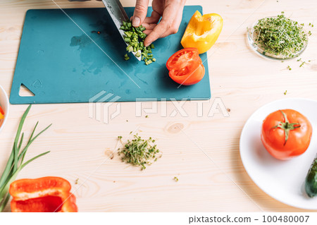 Lady cutting green onion for vegetable salad with microgreens Lady cutting green onion for vegetable salad with microgreens 100480007