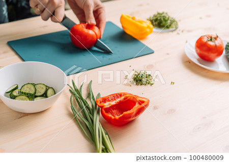 Lady cutting tomato for vegetable salad with microgreens Lady cutting tomato for vegetable salad with microgreens 100480009