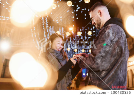 Holds gift box. Happy multiracial couple together outdoors in the city celebrating New year 100480526