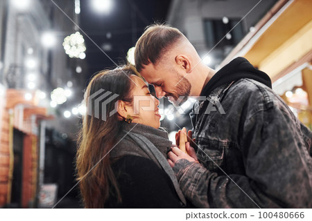 Embracing each other. Happy multiracial couple together outdoors in the city celebrating New year 100480666