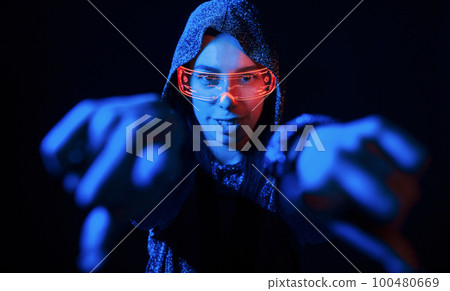 Does gestures by hands. Portrait of young girl that is in eyeglasses in blue neon lighting Does gestures by hands. Portrait of young girl that is in eyeglasses in blue neon lighting 100480669