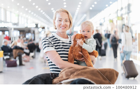 Mother traveling with child, holding his infant baby boy at airport terminal waiting to board a plane. Travel with kids concept 100480912