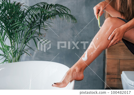 Beautiful young woman have free time at home in the bath. Shaves legs 100482017