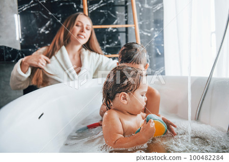 Having fun. Young mother helps her son and daughter. Two kids washing in the bath Having fun. Young mother helps her son and daughter. Two kids washing in the bath 100482284