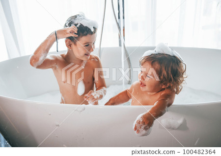 Two kids having fun and washing themselves in the bath at home Two kids having fun and washing themselves in the bath at home 100482364