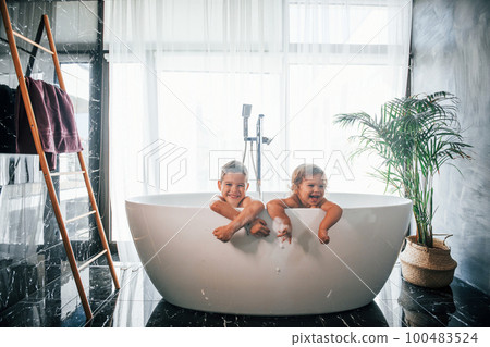 Two kids having fun and washing themselves in the bath at home. Posing for a camera 100483524