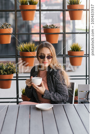 A beautiful pretty girl in a cafe drinking coffee on a summer terrace A beautiful pretty girl in a cafe drinking coffee on a summer terrace 100483937