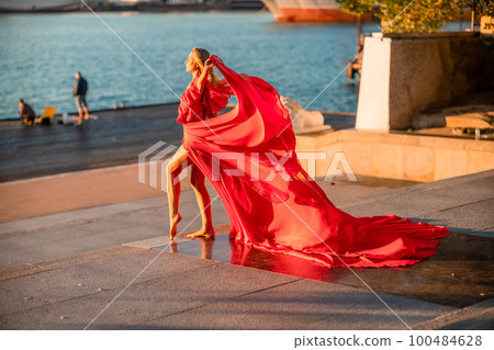 Sunrise red dress. A woman in a long red dress against the backdrop of sunrise, bright golden light of the sun's rays. The concept of femininity, harmony. 100484628