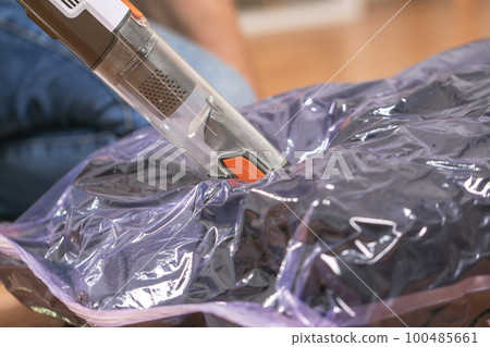 A man removes air from a vacuum bag using a manual 100485661