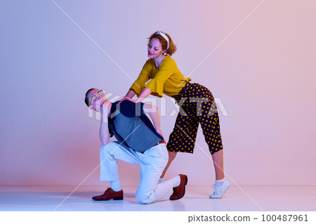Emotional young couple, man and woman in stylish clothes dancing retro dance against gradient pink purple studio background 100487961