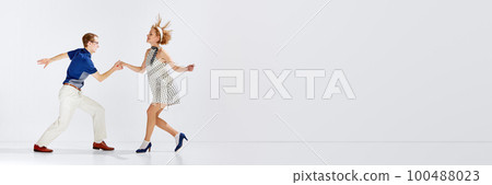 Active hobby. Young man and woman in stylish clothes dancing retro dance against grey studio background. Banner 100488023