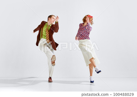 Young man and woman in stylish bright colorful clothes dancing retro dance against grey studio background Young man and woman in stylish bright colorful clothes dancing retro dance against grey studio background 100488029