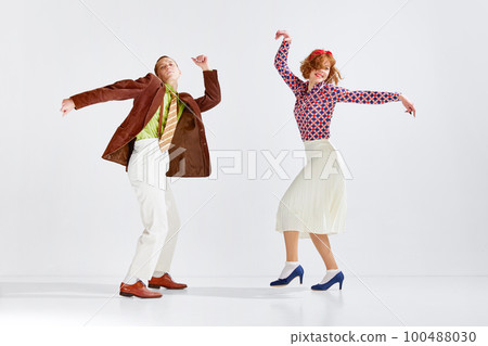 Young man and woman in stylish colorful clothes dancing retro dance against grey studio background. Active hobby Young man and woman in stylish colorful clothes dancing retro dance against grey studio background. Active hobby 100488030