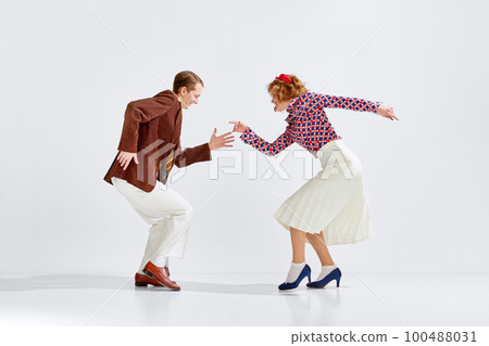 Old-school party. Young cheerful man and woman in stylish clothes dancing retro dance against grey studio background Old-school party. Young cheerful man and woman in stylish clothes dancing retro dance against grey studio background 100488031