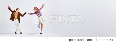Happy young man and woman in stylish clothes emotionally dancing retro dance against grey studio background Happy young man and woman in stylish clothes emotionally dancing retro dance against grey studio background 100488034