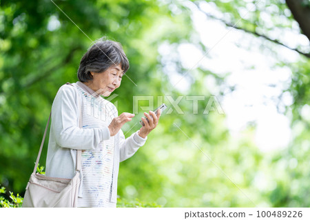A senior woman who operates a smartphone, an old woman who touches a smartphone outdoors 100489226