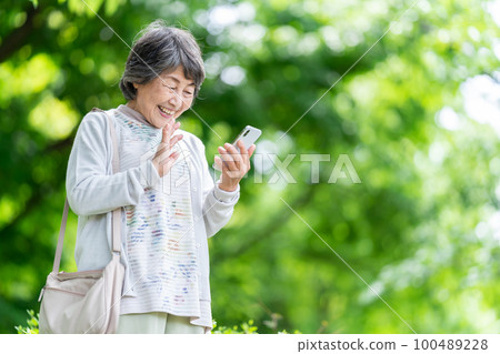 A senior woman who operates a smartphone, an old woman who touches a smartphone outdoors 100489228