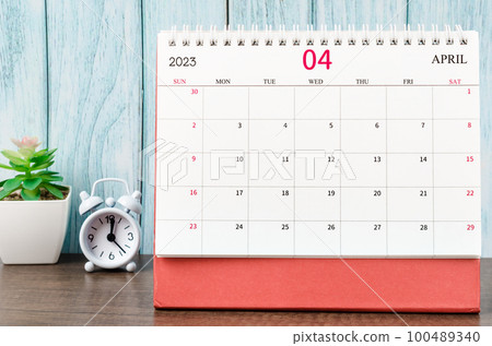 The April 2023 Monthly desk calendar for the organizer to plan 2023 year with alarm clock on wooden table. 100489340