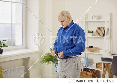 Senior man measuring waist with tape at home Senior man measuring waist with tape at home 100491220