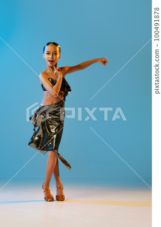 Expressive dance. Beautiful little girl in stage attire dancing latino madern ballroom dance over blue background. Music, dance, education, professional dance school concept 100491878