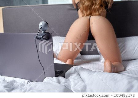 Beautiful, young girl posing in front of a web camera, working as a model. He takes off his bra. The concept of online flirting, sex on the Internet. 100492178