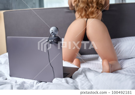 Beautiful, young girl posing in front of a web camera, working as a model. He takes off his bra. The concept of online flirting, sex on the Internet. 100492181