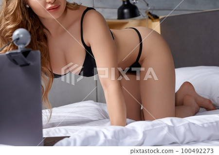 Beautiful, young girl posing in front of a web camera, working as a model. He takes off his bra. The concept of online flirting, sex on the Internet. Beautiful, young girl posing in front of a web camera, working as a model. He takes off his bra. The concept of online flirting, sex on the Internet. 100492273