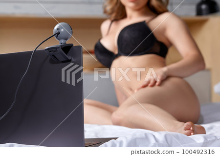 Beautiful, young girl posing in front of a web camera, working as a model. He takes off his bra. The concept of online flirting, sex on the Internet. Beautiful, young girl posing in front of a web camera, working as a model. He takes off his bra. The concept of online flirting, sex on the Internet. 100492316
