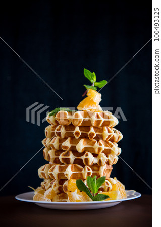 Cooked sweet Belgian waffles with oranges on a black 100493125