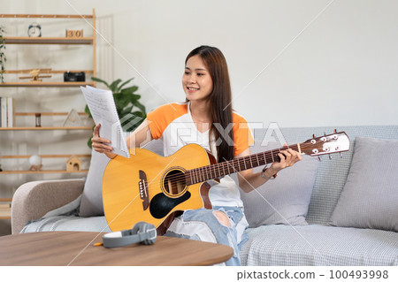 Young woman is holding a book of lyrics and chords to playing guitar and practice to singing the song 100493998