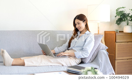 Female freelance is reading business data and typing information on laptop while sitting on comfortable Female freelance is reading business data and typing information on laptop while sitting on comfortable 100494029