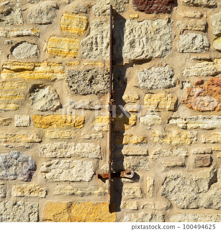 Sturdy yellow and beige cut stone wall and mounted piece of iron Sturdy yellow and beige cut stone wall and mounted piece of iron 100494625