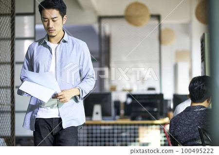young asian business man reviewing document while walking in office 100495222