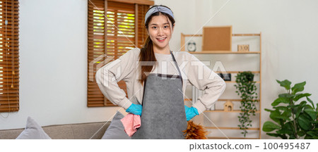 Housekeeper is wearing protective gloves to holding cloth and feather duster for cleanups to wiping dirt Housekeeper is wearing protective gloves to holding cloth and feather duster for cleanups to wiping dirt 100495487