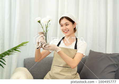 Housekeeper is wearing protective gloves and using microfiber cloth to cleanups and wiping dirt on glass vase 100495777