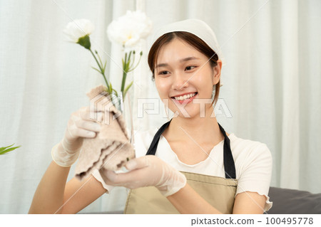 Housekeeper is wearing protective gloves and using microfiber cloth to cleanups and wiping dirt on glass vase 100495778