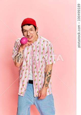 Funny stylish guy with tattoo puffing up the balloon like cigarettes and looking at camera over pink background. Concept of human emotions, fashion, youth, student life 100499189