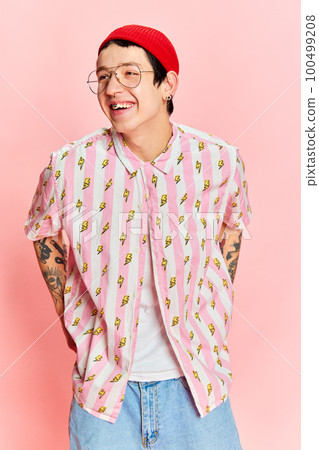 Portrait of fashionable modern stylish guy wearing glasses keeping hands in pockets and looking away isolated on pink background. 100499208