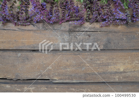 Lavender and sage flowers on a wooden table close-up. Horizontal planks of dark old wood with purple and blue flowers and leaves around the edges. Still life and flat lay. Free copy space for text 100499530