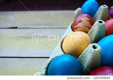 Multi-colored eggs painted with gouache and onion peel in a cardboard box on a wooden table background. Ten boiled eggs. Postcard poster for Easter. Easter holiday. Red, blue, yellow, brown eggs Multi-colored eggs painted with gouache and onion peel in a cardboard box on a wooden table background. Ten boiled eggs. Postcard poster for Easter. Easter holiday. Red, blue, yellow, brown eggs 100499664