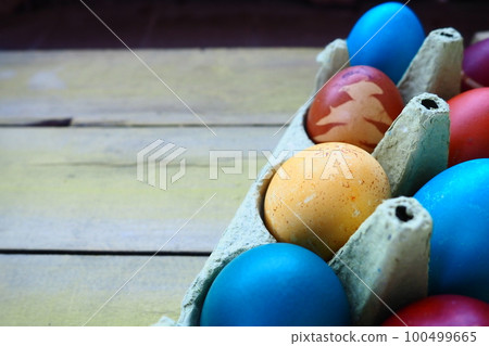 Multi-colored eggs painted with gouache and onion peel in a cardboard box on a wooden table background. Ten boiled eggs. Postcard poster for Easter. Easter holiday. Red, blue, yellow, brown eggs Multi-colored eggs painted with gouache and onion peel in a cardboard box on a wooden table background. Ten boiled eggs. Postcard poster for Easter. Easter holiday. Red, blue, yellow, brown eggs 100499665