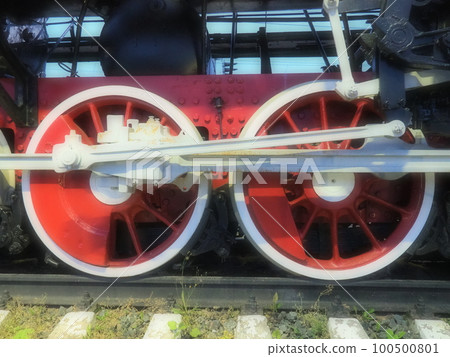 Retro vintage wheels of a locomotive or train close up. Red large heavy metal wheels with piston guiding mechanisms. Locomotive of the 19th - 20th centuries with a steam engine. Blurred soft focus Retro vintage wheels of a locomotive or train close up. Red large heavy metal wheels with piston guiding mechanisms. Locomotive of the 19th - 20th centuries with a steam engine. Blurred soft focus 100500801