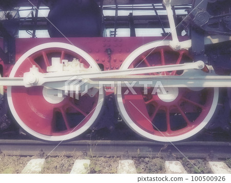Retro vintage wheels of a locomotive or train close up. Red large heavy metal wheels with piston guiding mechanisms. Locomotive of the 19th - 20th centuries with a steam engine. Blurred soft focus 100500926
