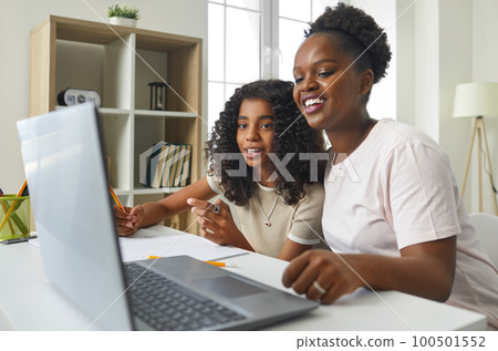 Caring African American mother using laptop to help her daughter with school homework. 100501552