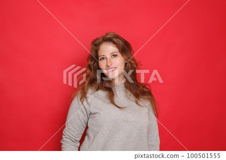 Attractive brunette woman in grey sweater on red studio wall  background 100501555