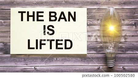 Text The ban is removed written on a sticker, on a wooden table a light bulb Text The ban is removed written on a sticker, on a wooden table a light bulb 100502580