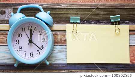 On a wooden table, a sticker without an inscription and an alarm clock 100502596