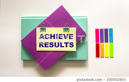 achieve results, text is written on a sticker. Colored notepads lie on a white achieve results, text is written on a sticker. Colored notepads lie on a white 100502601