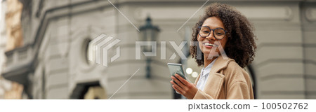 Smiling woman after shopping with paper bags and phone while standing in city 100502762